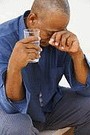 older man with headache holding a glass of water