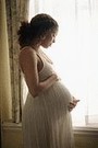 pregnant woman holding stomach, looking out of window