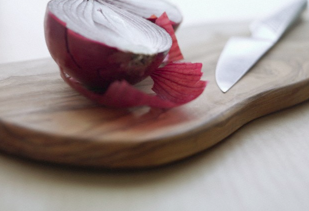 Half of a red onion sitting on a cutting board beside a knife