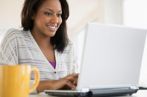 A woman typing on her laptop with a yellow coffee mug beside her
