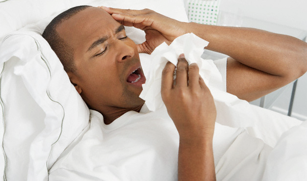A man holding tissue as he sneezes while lying in his bed