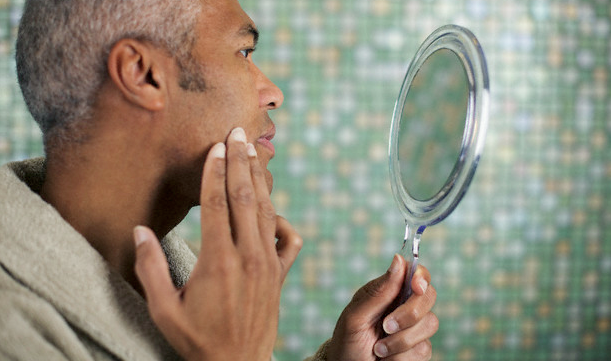 A man using a handheld mirror to examine his skin
