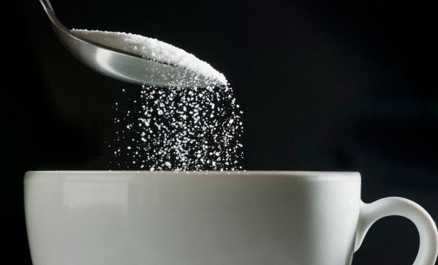 A spoonful of sugar being added to a cup