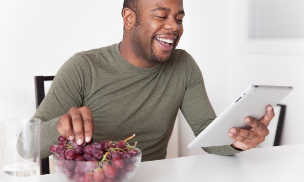 A man eating grapes and reading his iPad