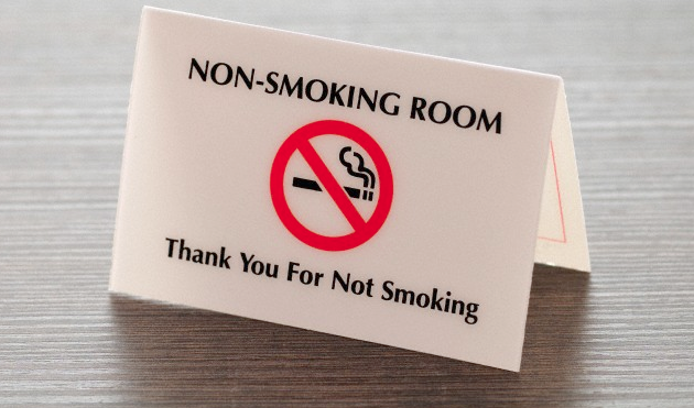 A no-smoking hotel room sign sitting on a wooden desk surface