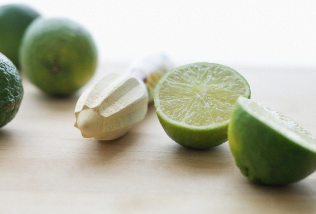 Three limes and a juicer sitting on a wooden surface