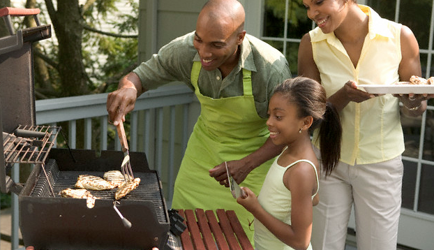 A family standing with plates in front of a grill