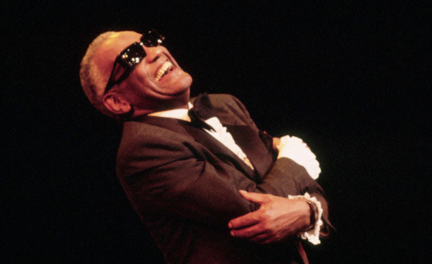 An image of Ray Charles, smiling, with his arms wrapped around himself