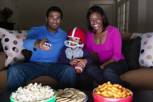 A family watching football on TV with snacks on a table