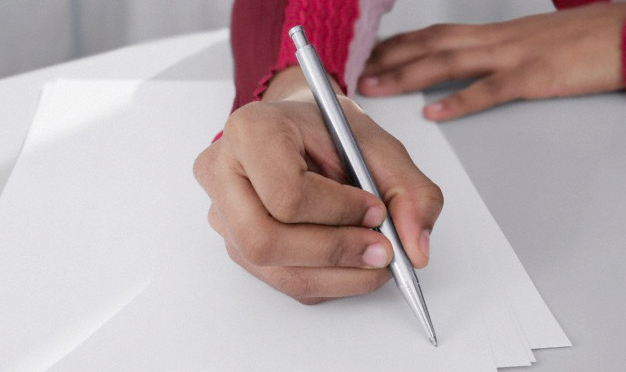 A close-up of a woman's hand holding a pen over pieces of paper