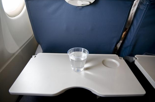 A cup of water sitting on airplane tray table