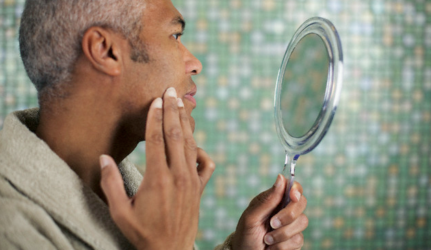 A man looking at a patch of his skin using a handheld mirror