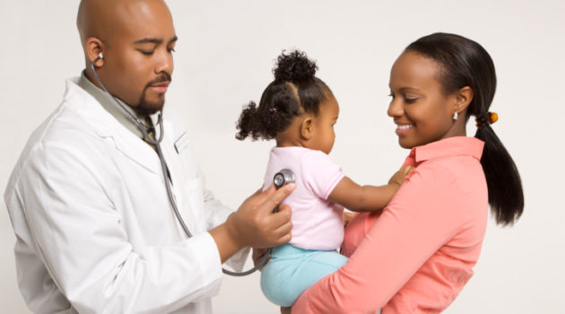 African-American male pediatrician examining baby girl being held by mother.