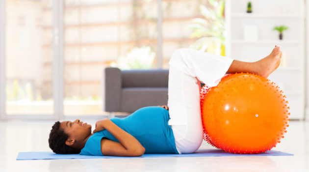 pregnant woman laying on floor with her feet up on a exercise ball