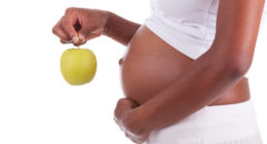 Young pregnant black woman holding a green apple