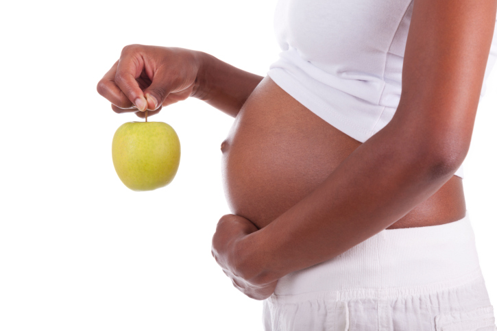 Young pregnant black woman holding a green apple