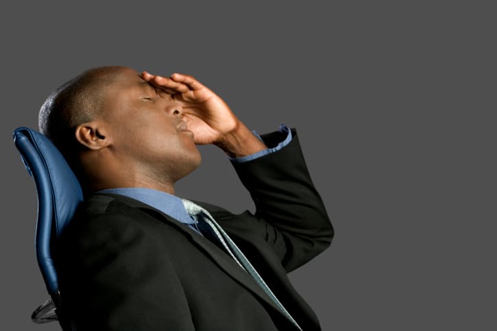 Businessman leaning back in chair with hand on forehead