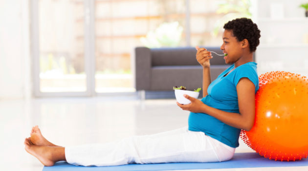 pregnant african american woman eating healthy salad on exercise mat