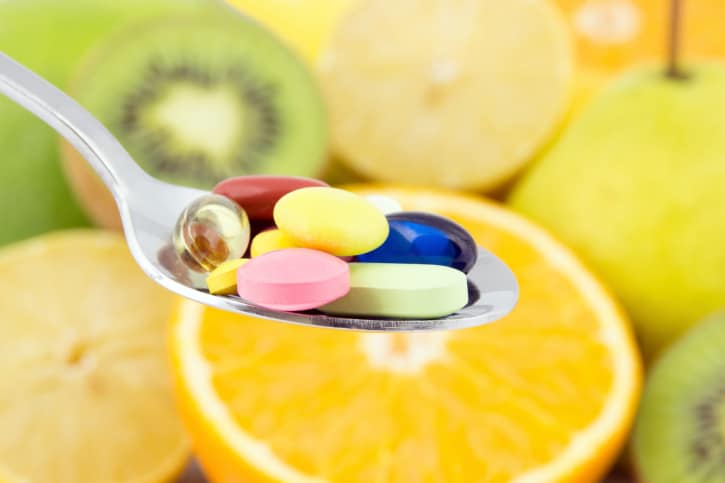 spoonful of different pills, different fruits in background