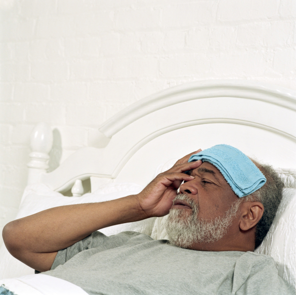 African American Black Senior man lying in bed, holding flannel to forehead, close-up