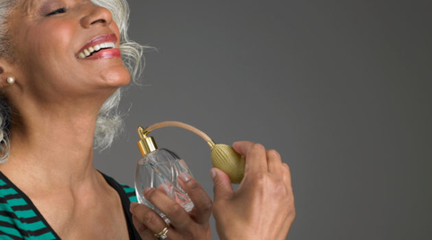 older woman spraying perfume on neck and smiling
