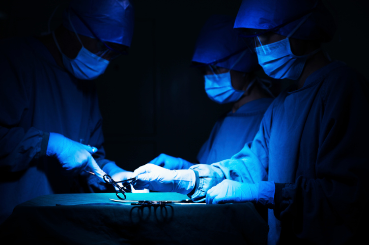 Surgeons holding surgical equipment at the operating table and working