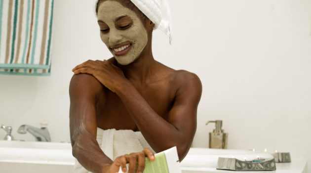 woman with face mask putting on lotion