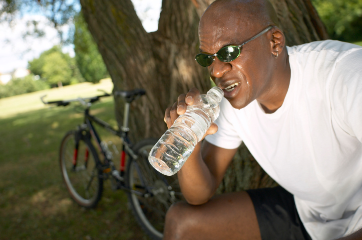 black man drinking water next to bike