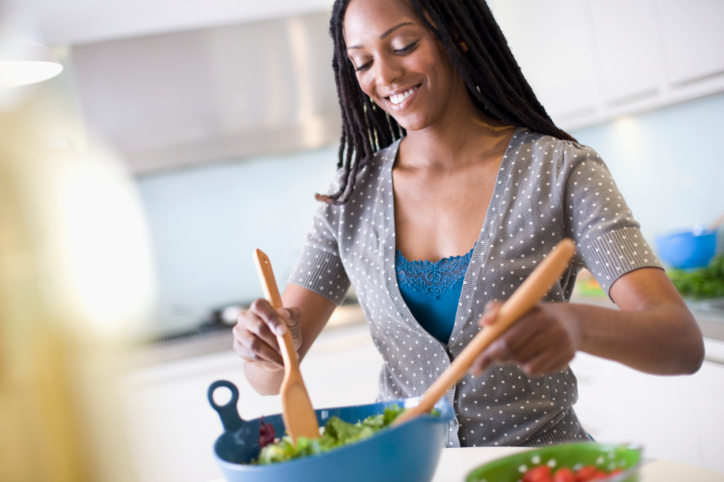 African American Black woman in kitchen mixing salad