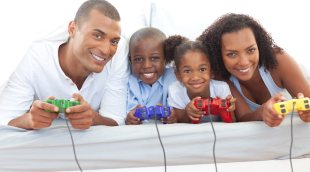 African American Black Animated family playing video game lying down on bed