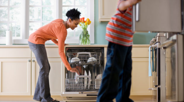 African American Black Woman Unloading Dishwasher While Son Looks in Refrigerator in kitchen