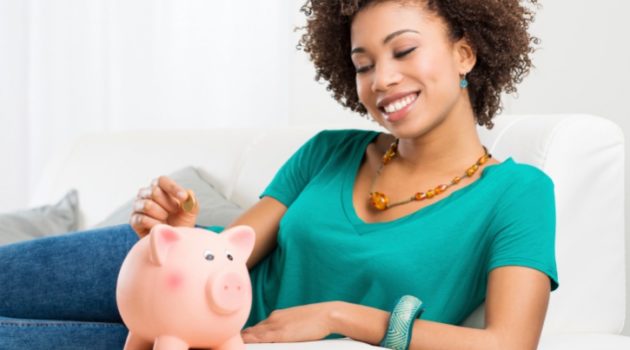 African American Woman on couch Putting Coin In Piggybank