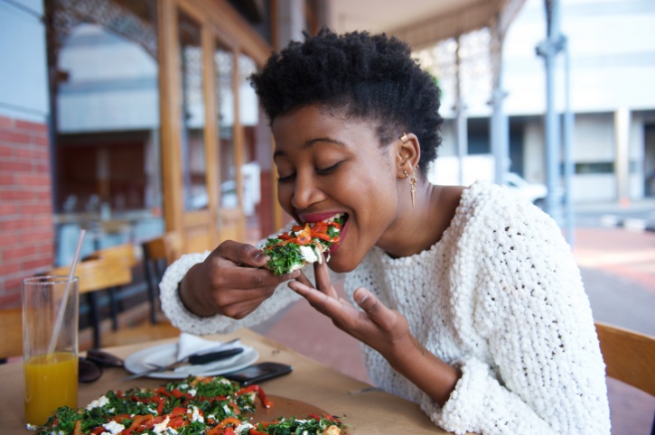 African American woman eating pizza outside