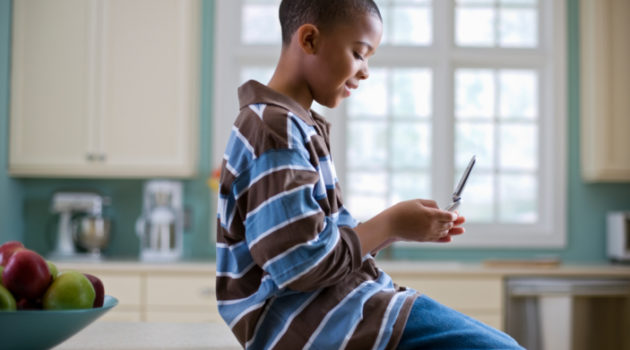 young African American boy sitting in kitchen looking at cell phone
