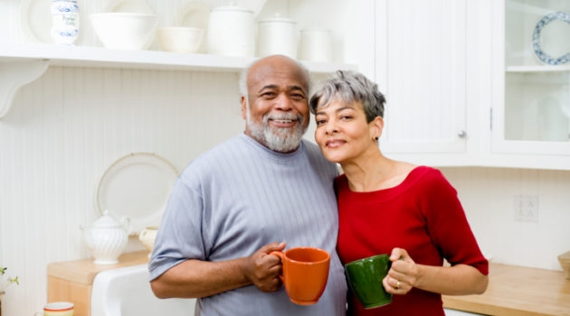 African American senior couple in kitchen hugging with coffee mugs