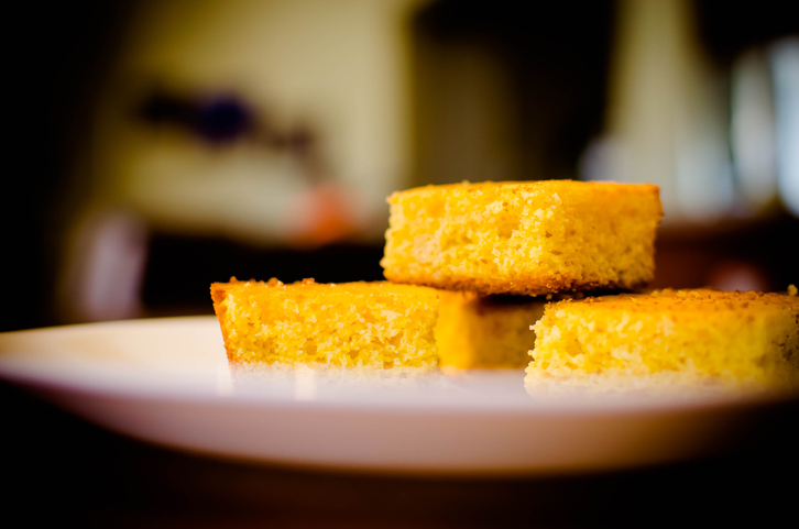Yellow corn bread on a white plate. Kitchen in background.