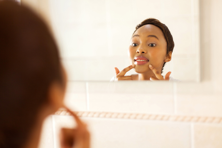 African American woman checking face for pimples in mirror