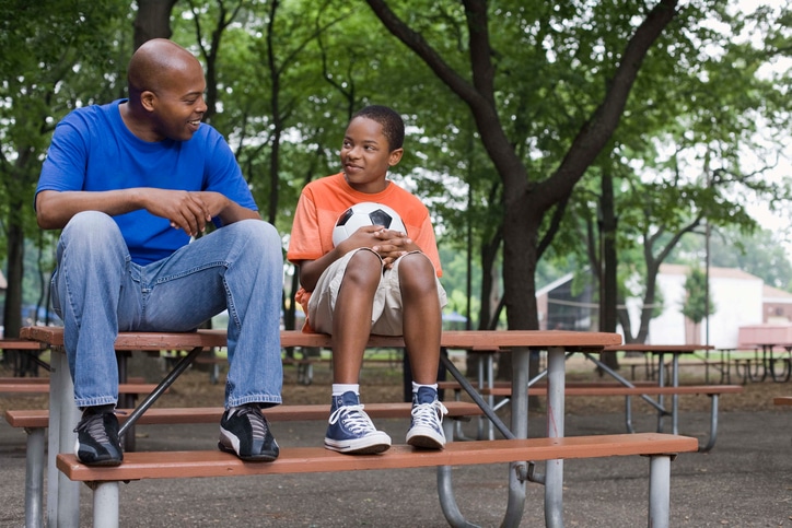 African American man and boy sitting outside on picnic table