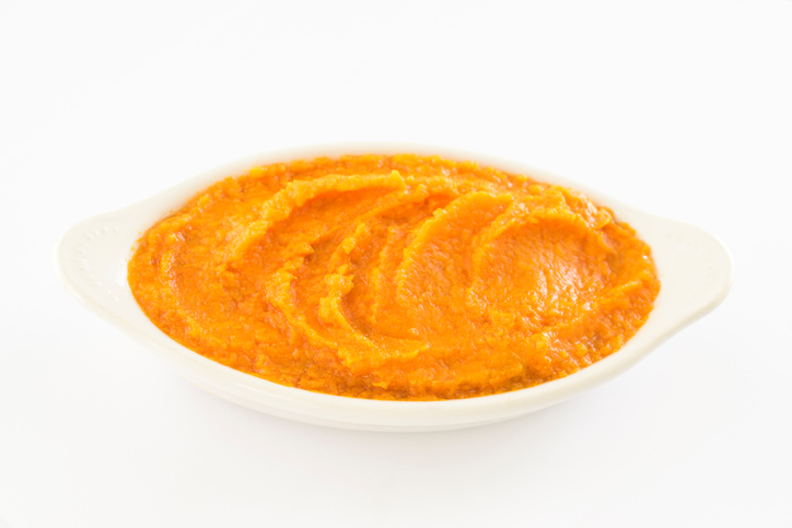 Baked sweet potato that has been mashed and served in a white dish on a white background