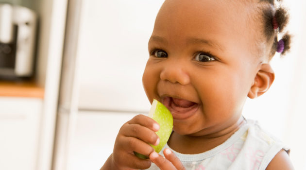 African American baby girl eating apple slice