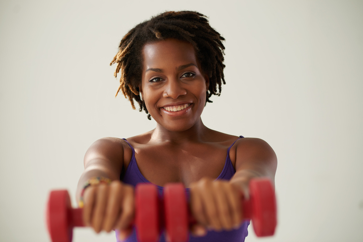 Cheerful healthy young woman exercising with dumbbells