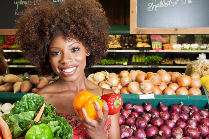 African American woman holding bell peppers and vegetables at supermarket