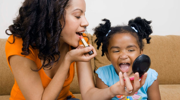 African american mother and daughter putting on lipstick makeup