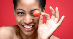 African American woman holding strawberry by eye