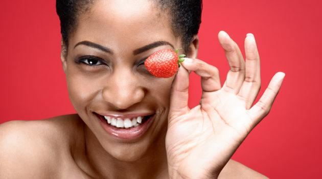African American woman holding strawberry by eye