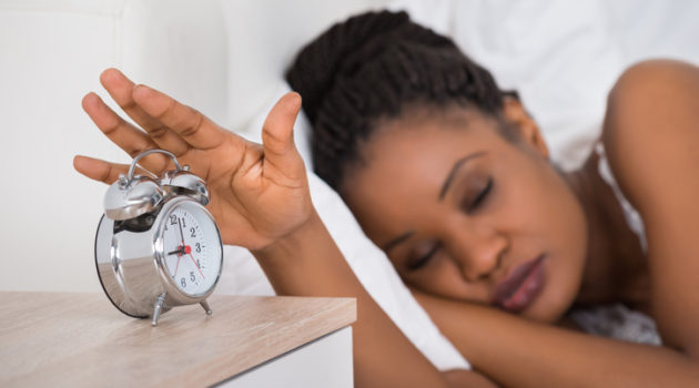 African American woman sleeping in bed hitting alarm