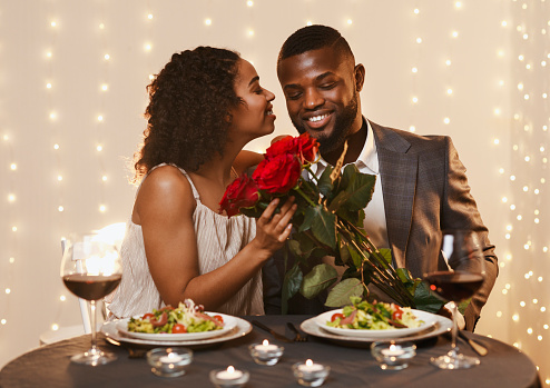 Thankful black lady holding bunch of roses, kissing her boyfriend