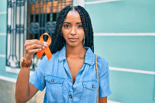Young african american woman with relaxed expression holding orange ribbon at the city.