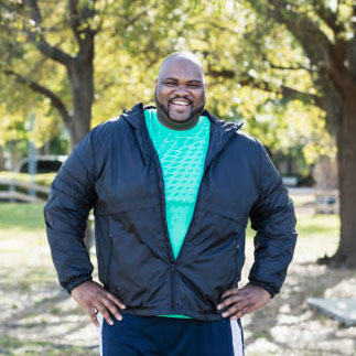 A mature African-American man in his 40s with shaved head, mustache and beard, smiling at the camera. He has a large build.